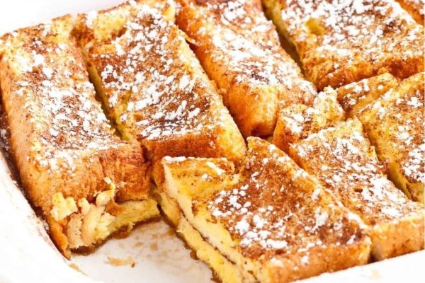 French toast casserole in a white dish with powdered sugar.