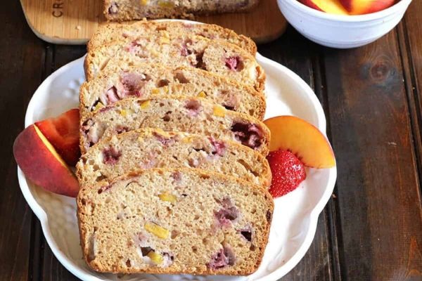 Sliced bread with strawberries and peaches on a plate.