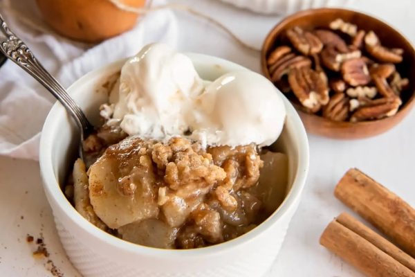 Apple crisp in a bowl with ice cream and pecans.