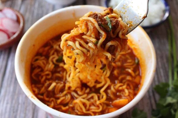 A spoon is being held over a bowl of ramen noodles.