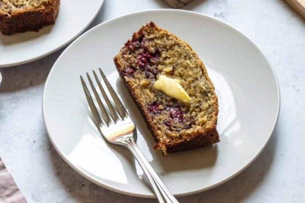 A slice of banana bread with butter on a plate.