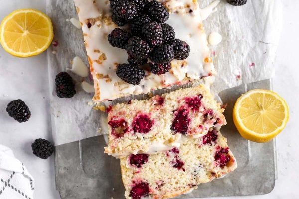 A slice of blackberry lemon loaf cake with lemon slices and blackberries.