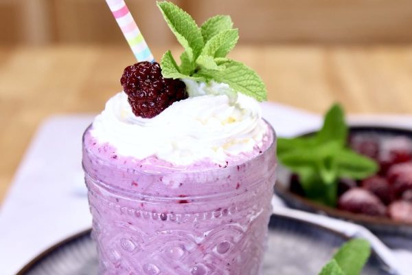 A refreshing blackberry smoothie topped with whipped cream and garnished with mint leaves.