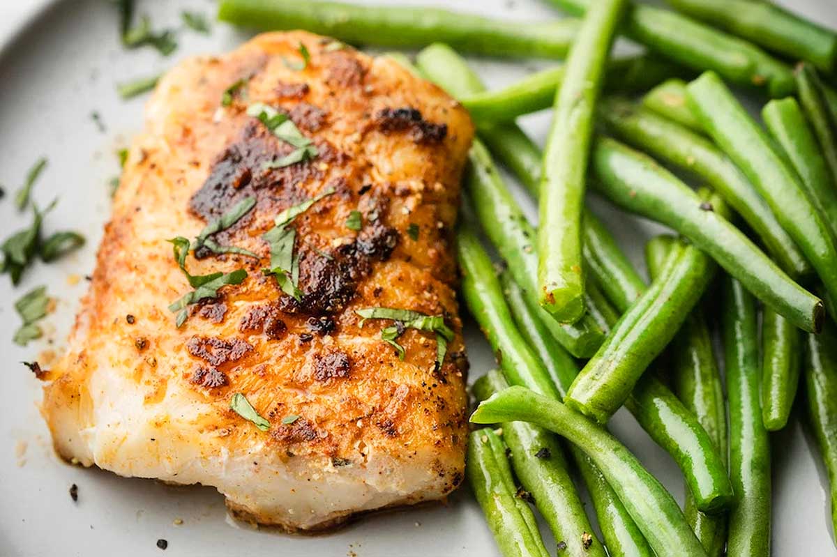 A piece of fish and green beans on a plate.