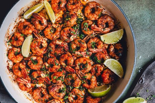 Shrimp in a skillet with lime wedges.