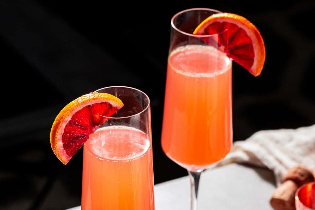 Two glasses of blood orange cocktails with a slice of orange and champagne.