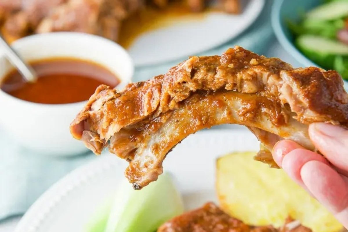 Slow Cooker Recipes featuring a hand holding a piece of ribs on a plate.