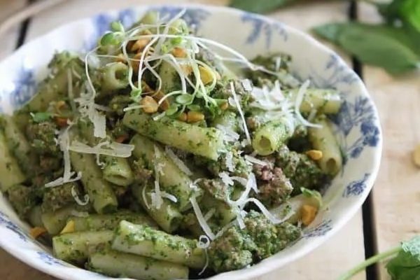 A bowl of Penne pasta with pesto and pine nuts.