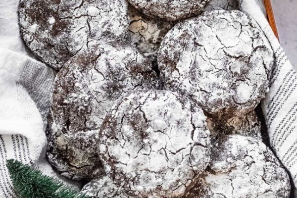 Delicious chocolate crinkle cookies are beautifully arranged in a festive basket, accompanied by a breathtaking Christmas tree.