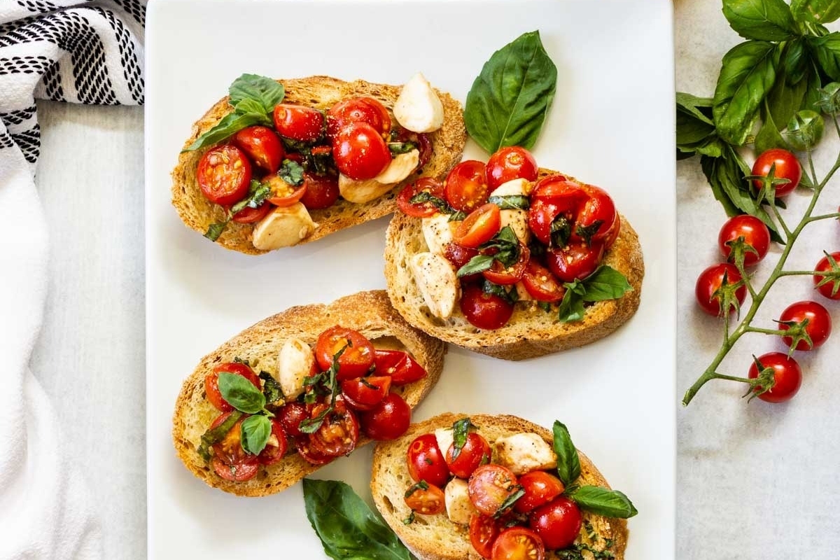 Italian bruschetta is a delightful appetizer consisting of four delectable bites featuring fresh tomatoes and fragrant basil atop a pristine white plate.