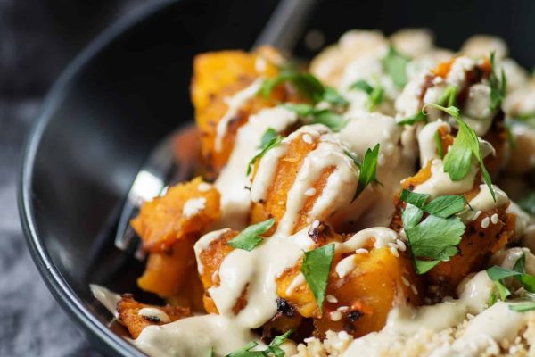 A colorful bowl of couscous with roasted squash and tahini sauce.