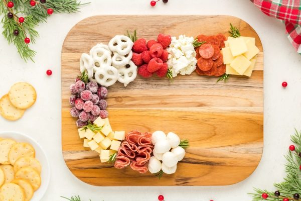 The letter c on a wooden charcuterie board adorned with cheese and crackers.