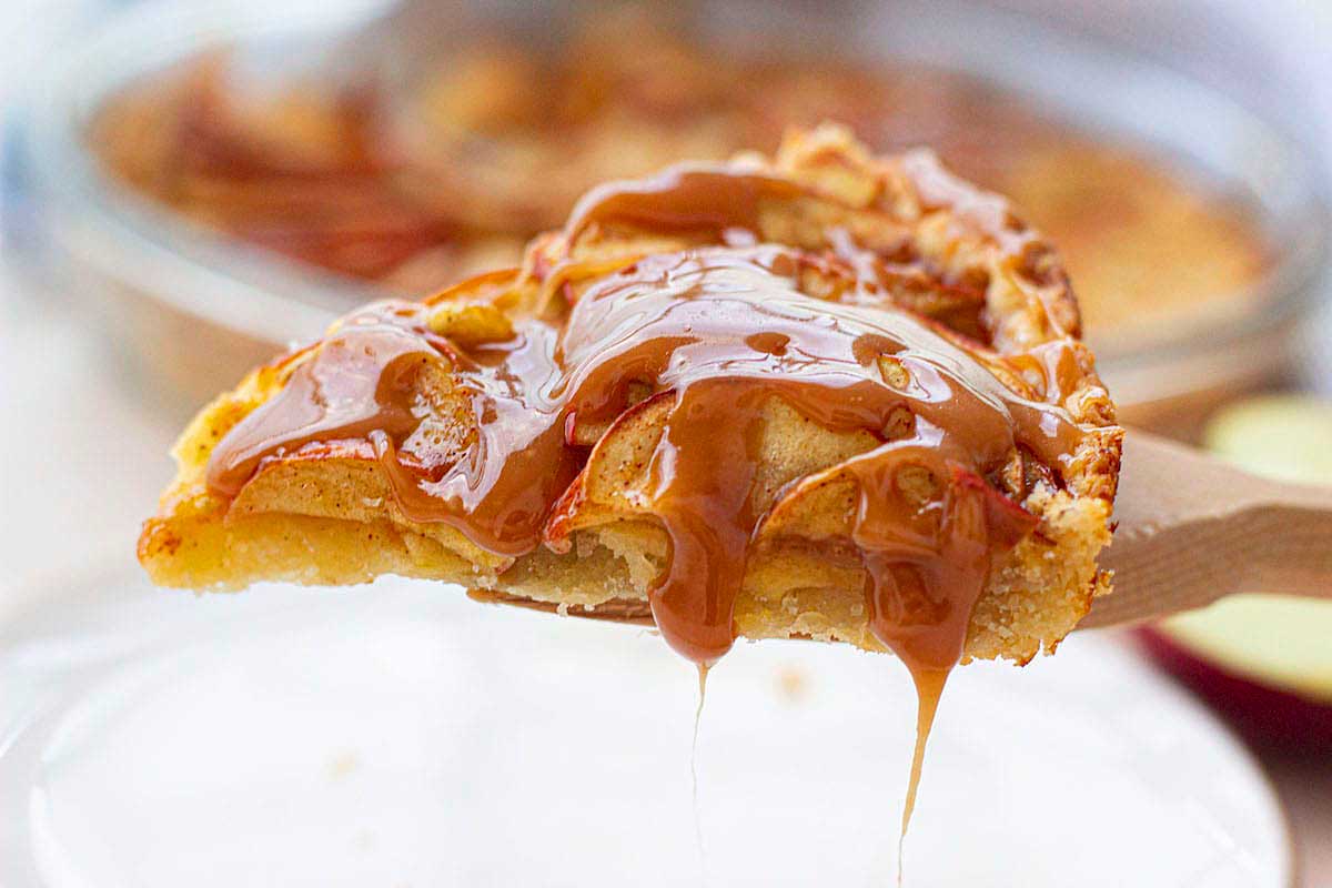 A slice of apple pie with caramel sauce on a wooden spoon.
