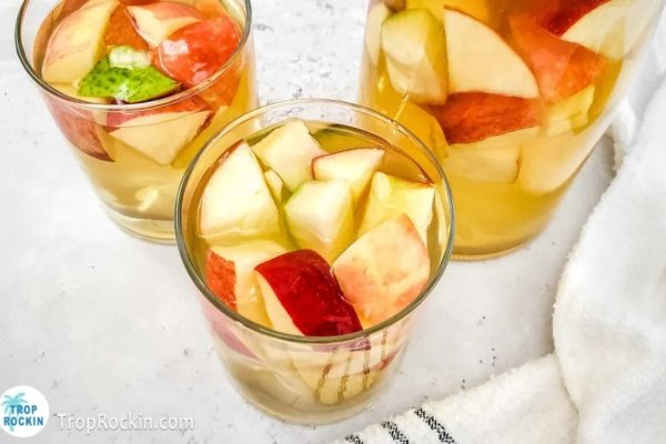 A glass of apple cider with slices of apples in it.