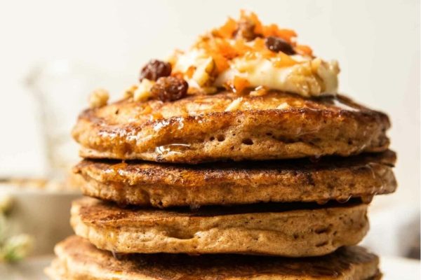 A stack of pancakes with raisins and nuts on top.