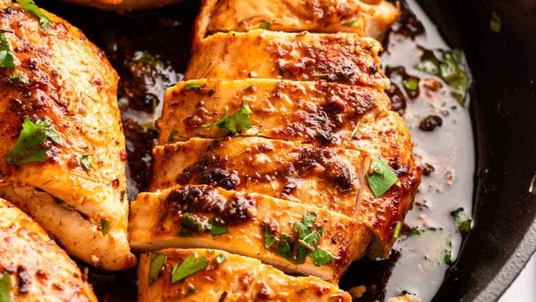 Chicken breasts in a skillet with herbs.