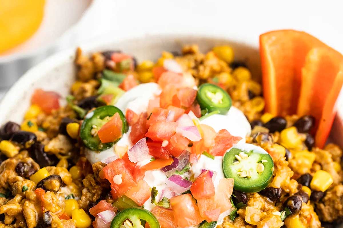 A bowl of mexican tacos with sour cream and salsa.