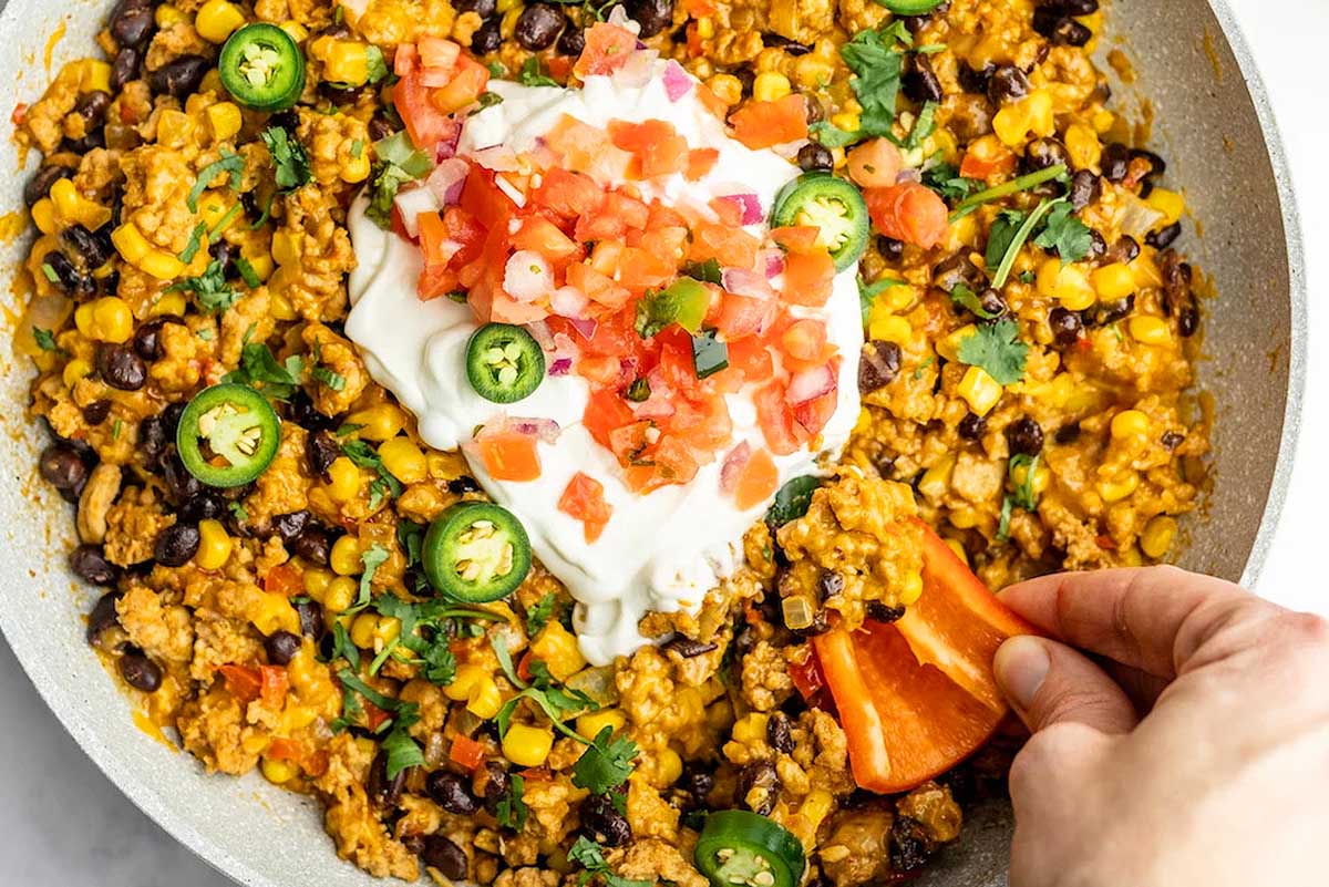 A person drizzling sour cream on a skillet of mexican rice.