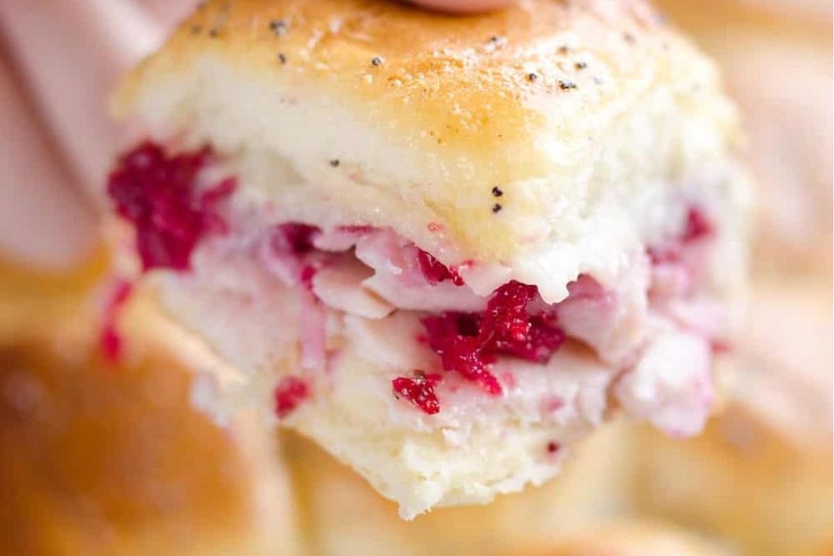 A person holding a delectable turkey and cranberry slider, perfect for making use of those leftover turkey recipes.