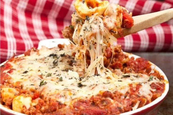 A wooden spoon is being used to eat a dish of lasagna.