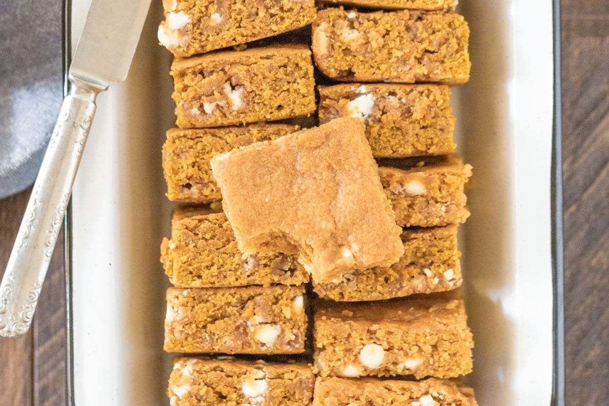 White chocolate pumpkin bars on a white plate with a knife.