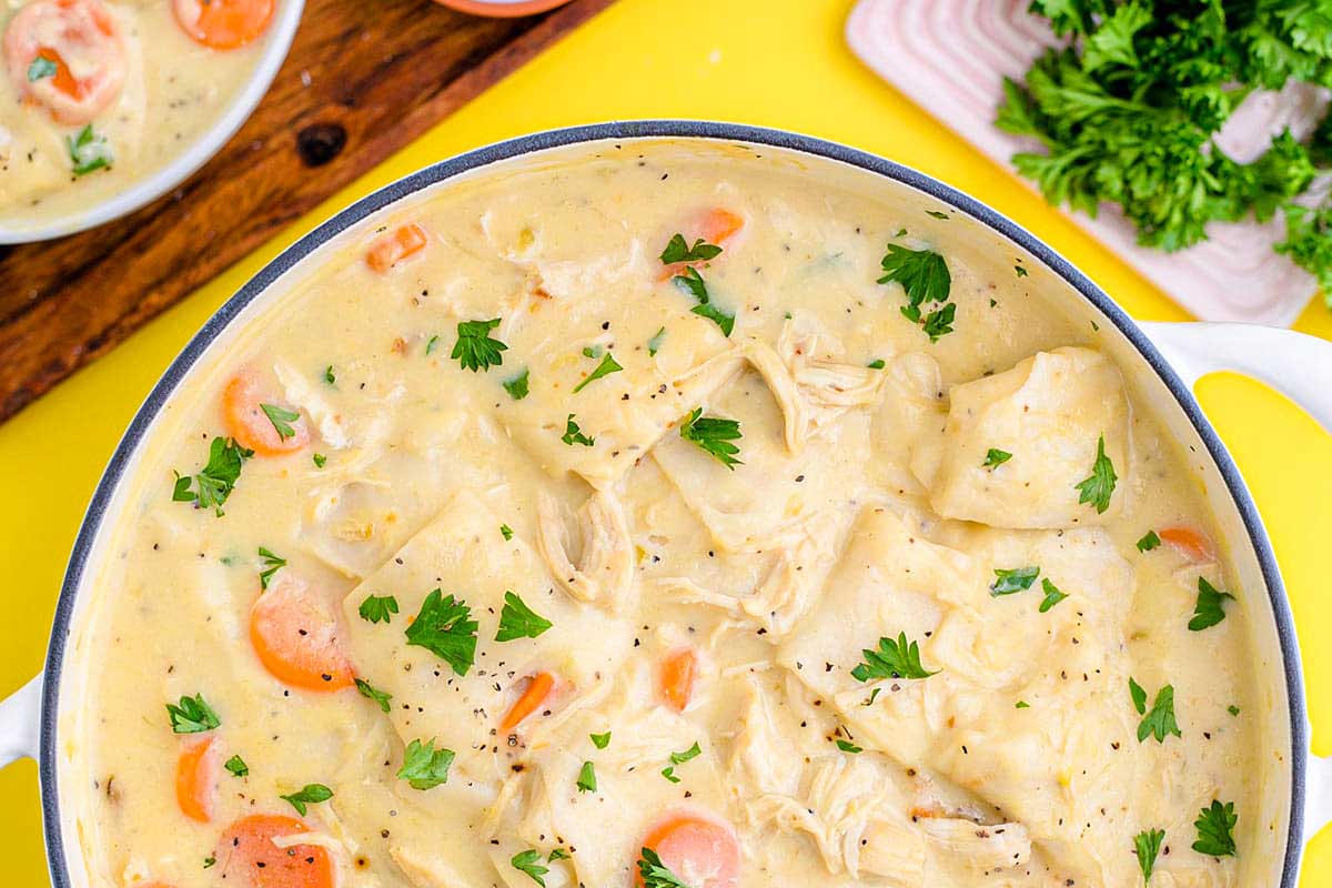 A bowl of chicken noodle soup with carrots and parsley.