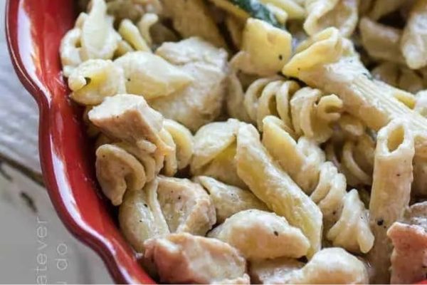 A red bowl of penne pasta with chicken and zucchini recipes.