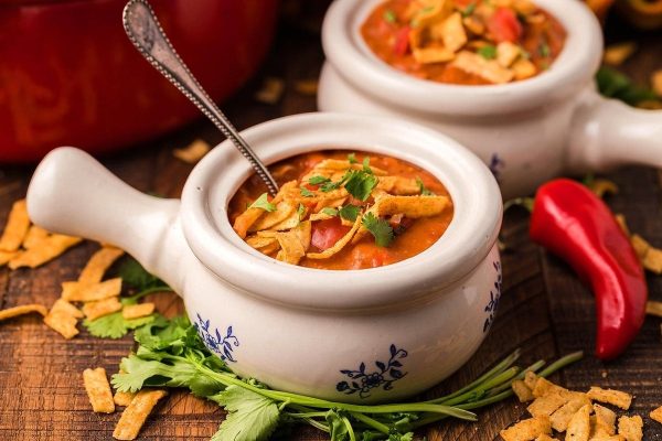 Two bowls of mexican chili soup on a wooden table.