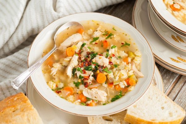 A bowl of chicken soup on a wooden table.