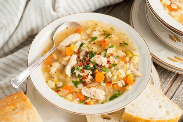 A bowl of chicken and rice soup on a wooden table.