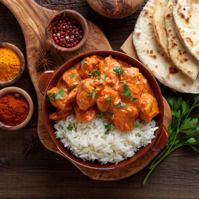 Chicken tikka masala spicy curry meat food in a clay plate with rice and naan bread on wooden background.