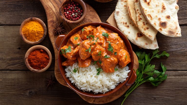 Chicken tikka masala spicy curry meat food in a clay plate with rice and naan bread on wooden background.