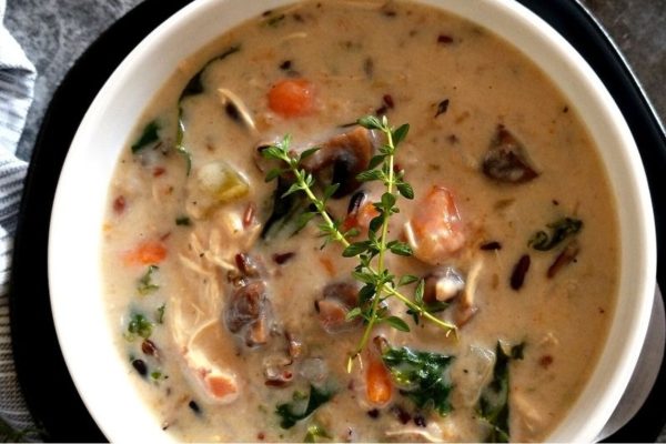 A bowl of chicken and wild rice soup with sprigs of thyme.