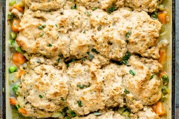 Chicken and dumplings in a baking dish with carrots and peas.
