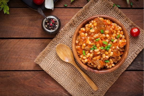 A bowl of beans and meat on a wooden table.