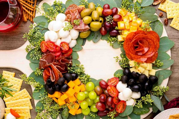 A festive Christmas charcuterie board adorned with a wreath of fruit and cheese, elegantly displayed on a wooden board.