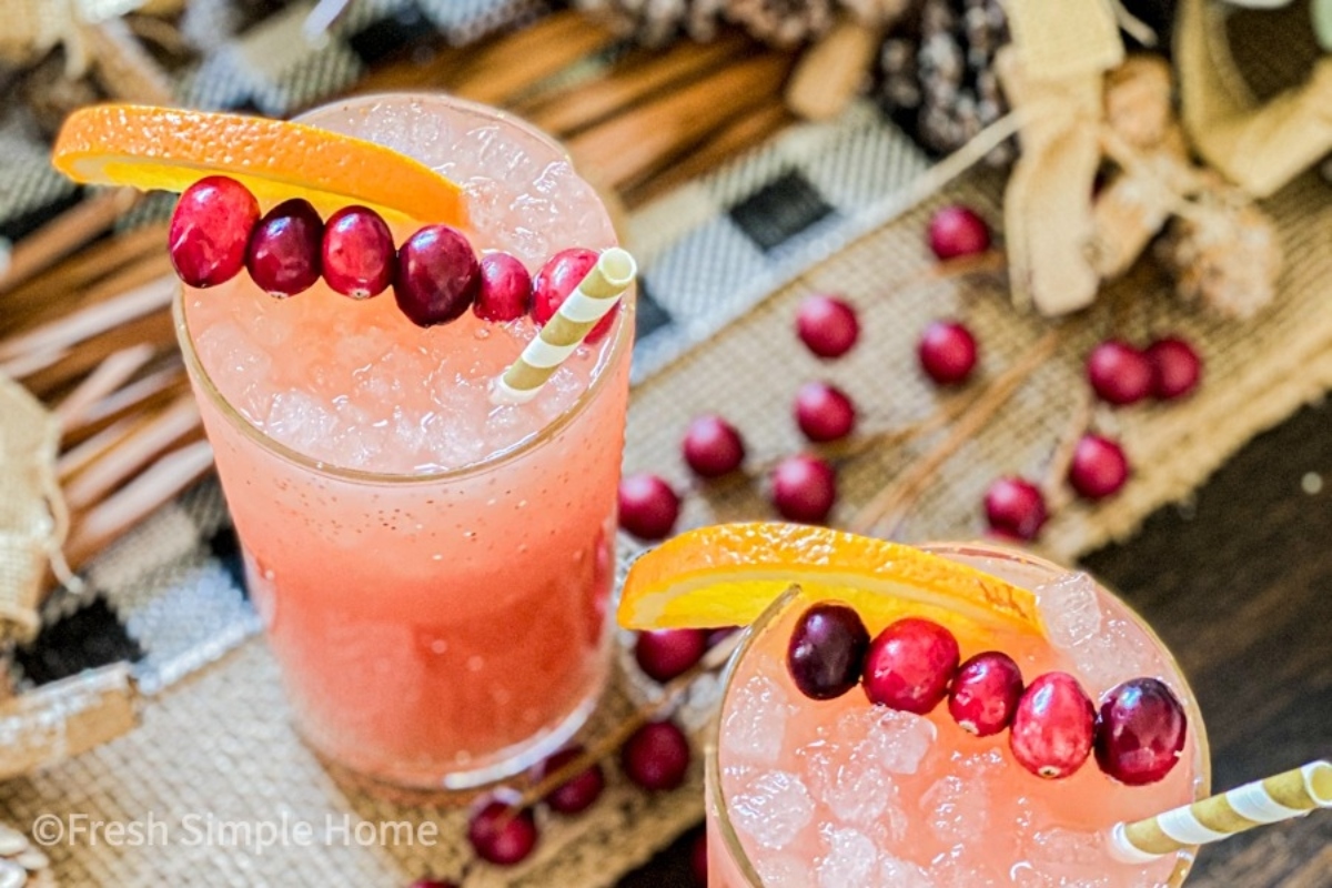 Two champagne cocktails with cranberries and oranges on a table.