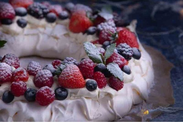 A traditional pavlova dessert topped with fresh berries and icing, perfect for Christmas celebrations.