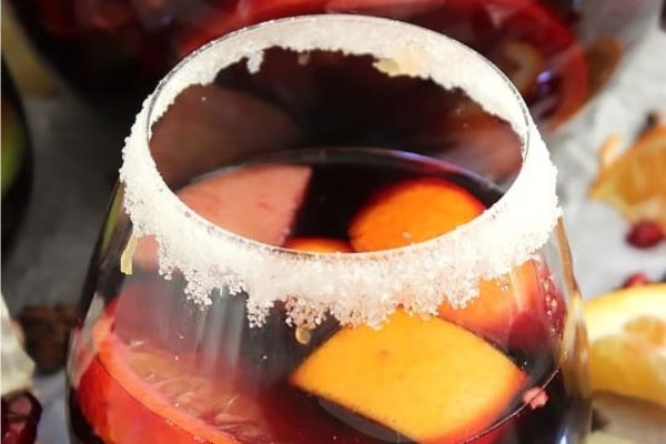 A glass of sangria with oranges and pomegranates.
