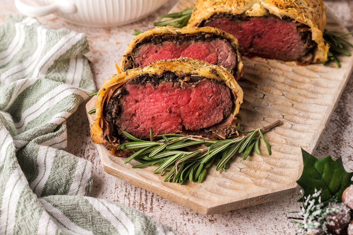 Beef wellington on a wooden board with rosemary sprigs.