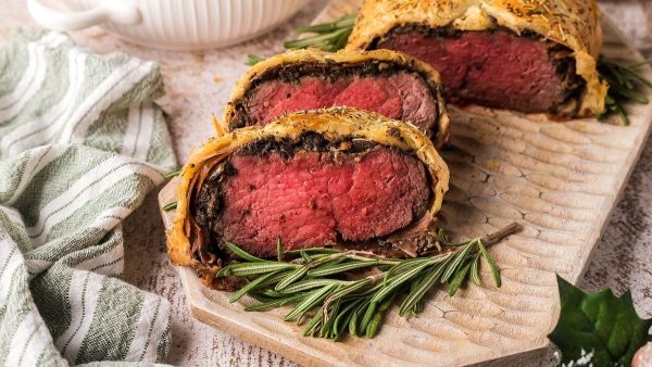 Beef wellington on a wooden board with rosemary sprigs.