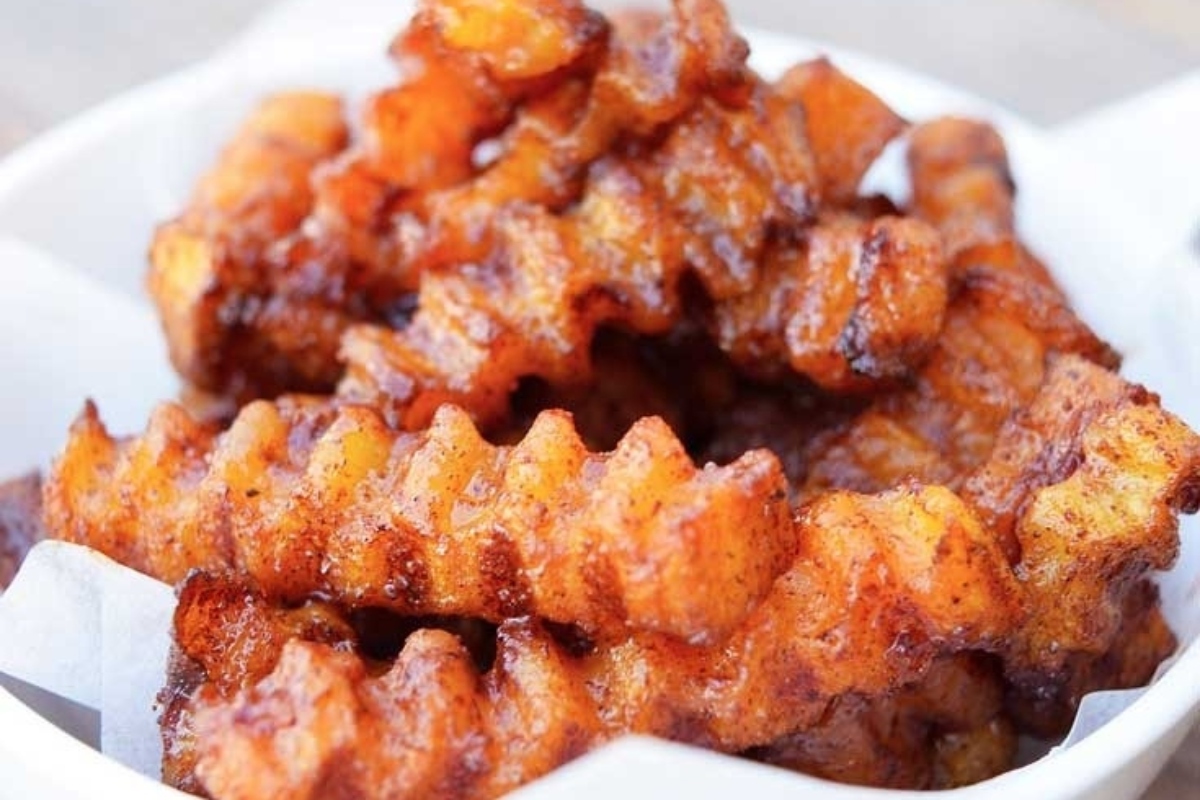 A bowl full of fried potato wedges placed deliciously on top of a wooden table.