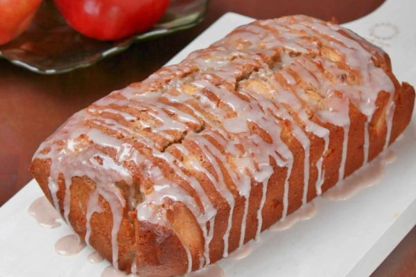 A loaf of bread with icing and apples on a plate.
