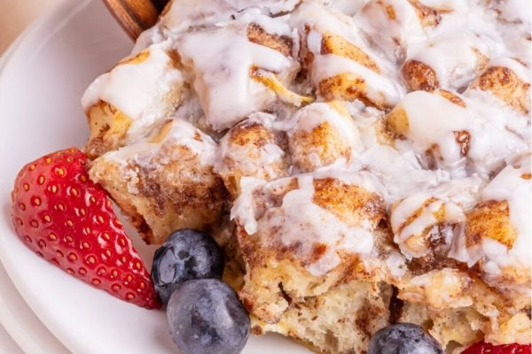 A plate with a cinnamon roll covered in icing and berries.