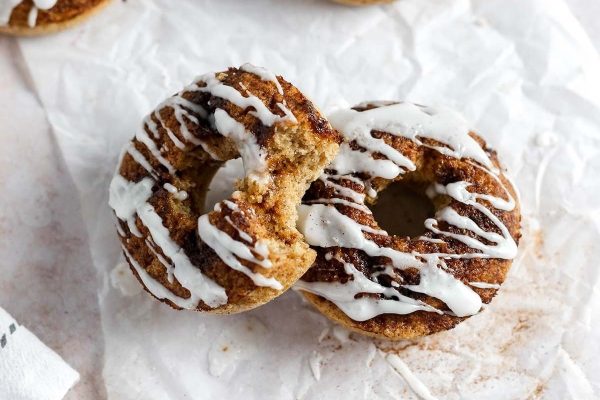 Two cinnamon donuts with icing on a piece of paper.