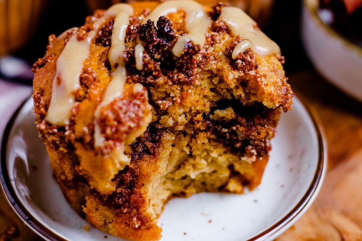 A cinnamon muffin with a bite taken out of it, resting on a plate.