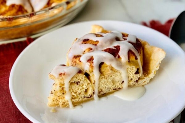 A slice of cinnamon roll pie with icing on a plate.