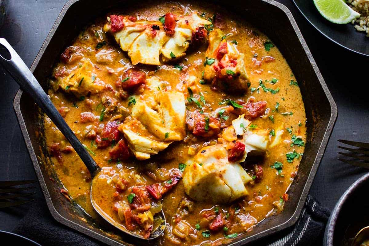 A bowl of curry with a spoon on a black table.