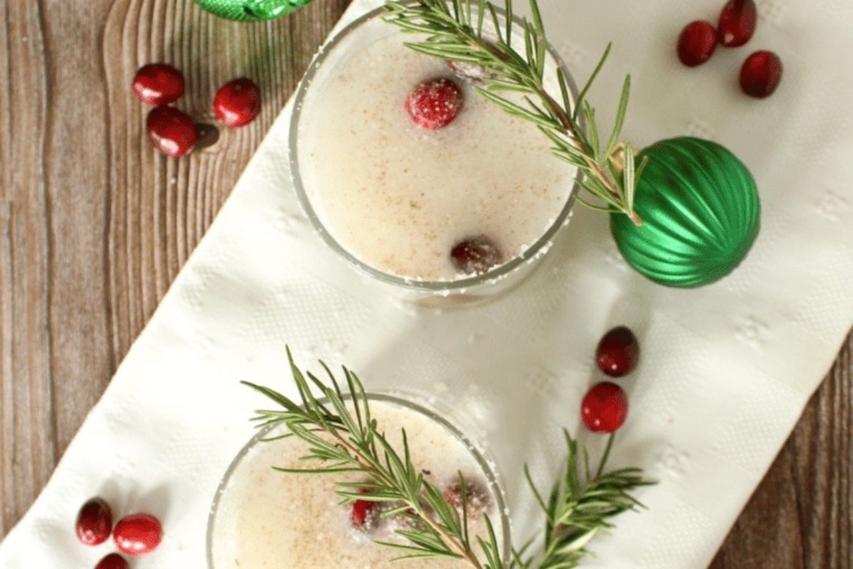 Two Christmas cocktails garnished with cranberries and sprigs of rosemary.