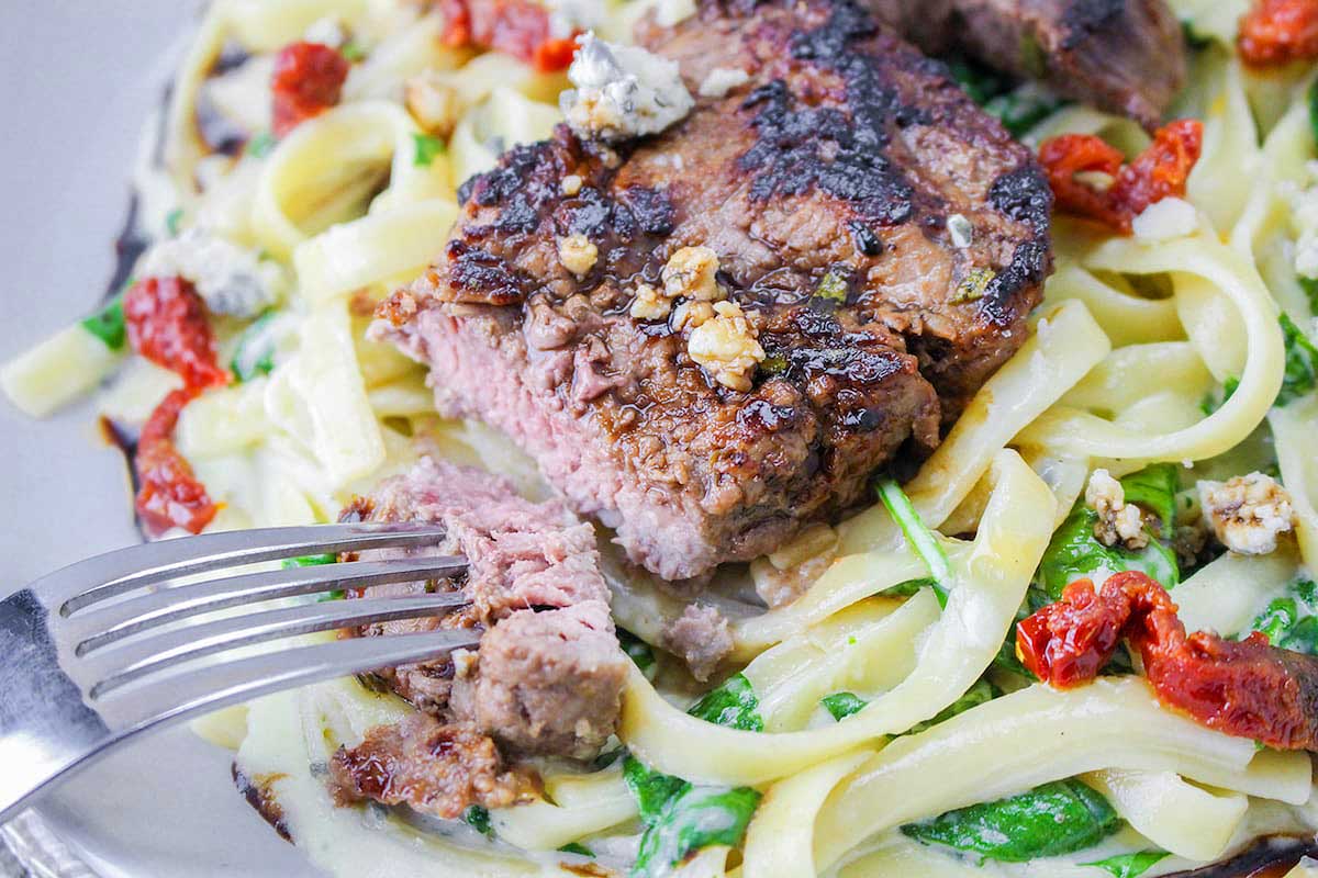 A plate of pasta with steak and spinach.